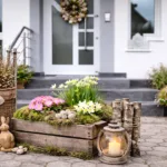 Frühlingsdeko am Hauseingang mit Holz, Blumen, Osterhasen und Türkranz auf Steinweg