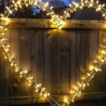 Garten im Februar Deko mit beleuchtetem Herz aus Lichterkette am Holzzaun in der Dämmerung