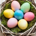 Bunt gefärbte Ostereier in einem Nest aus Zweigen und Moos auf hellem Holztisch