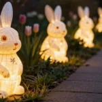 Leuchtende Osterhasen Figuren mit warmem Licht entlang eines Gartenwegs bei Abenddämmerung, umgeben von Tulpen und Frühlingspflanzen in natürlicher Gartenatmosphäre