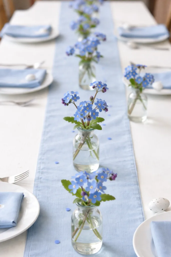 Tischdeko zu Ostern mit Blumen: kleine Glasvasen mit Vergissmeinnicht auf hellem Tischläufer arrangiert