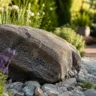 Großer Naturstein als Gartendeko im Beet mit Kies und Pflanzen im naturnahen Garten.