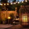 Gartendeko mit Licht auf gemütlicher Terrasse mit Laterne und warmen Lichterketten am Abend.