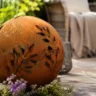 Rostige Gartendeko Kugel auf Holzterrasse mit Gräsern und Lavendel im Garten