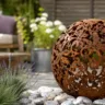 Gartendeko aus Metall mit rostiger Kugel auf moderner Terrasse zwischen Gräsern und Lavendel.