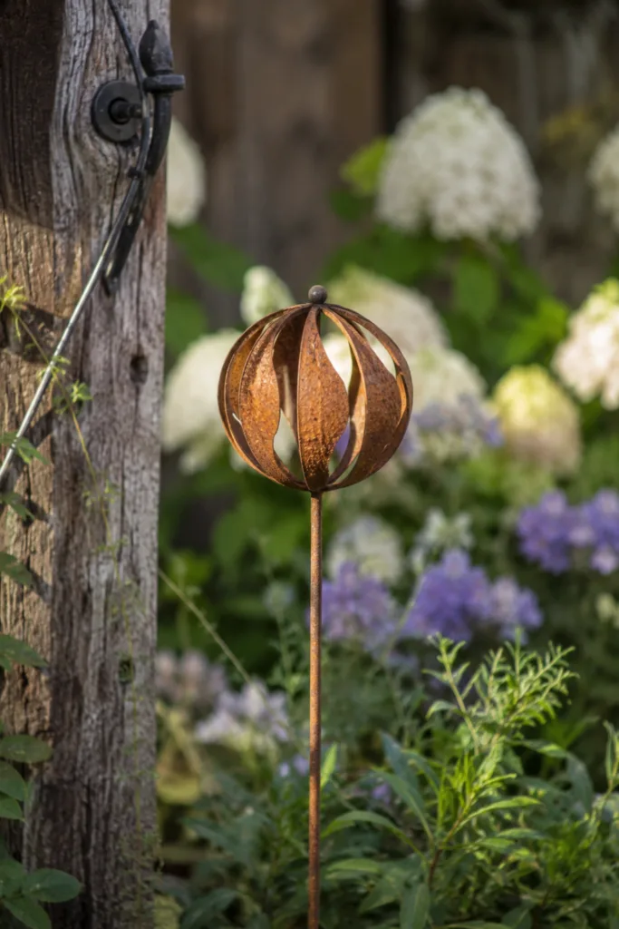 Rostige Gartenstecker zwischen Gräsern und Stauden als natürliche Gartendeko aus Rost.