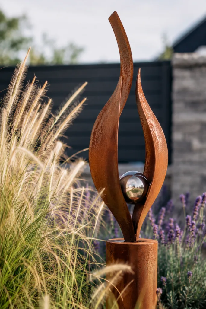 Moderne Gartendeko Figur aus Edelrost zwischen Gräsern und Lavendel als Blickfang im Garten.