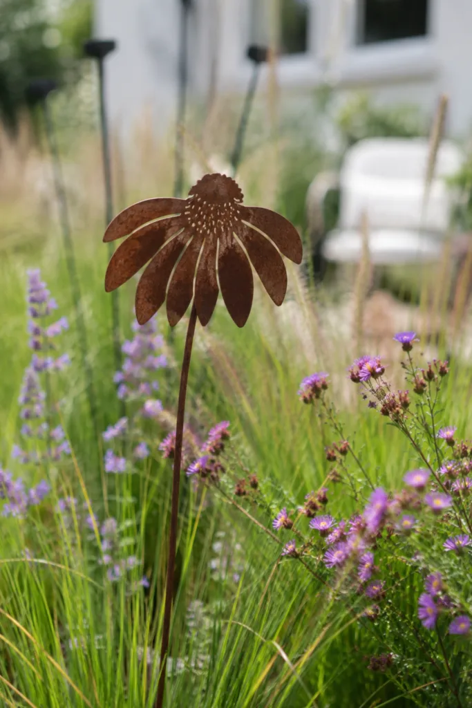 Gartendeko aus Metall mit rostigem Metallstecker zwischen Stauden und Ziergräsern im Garten.