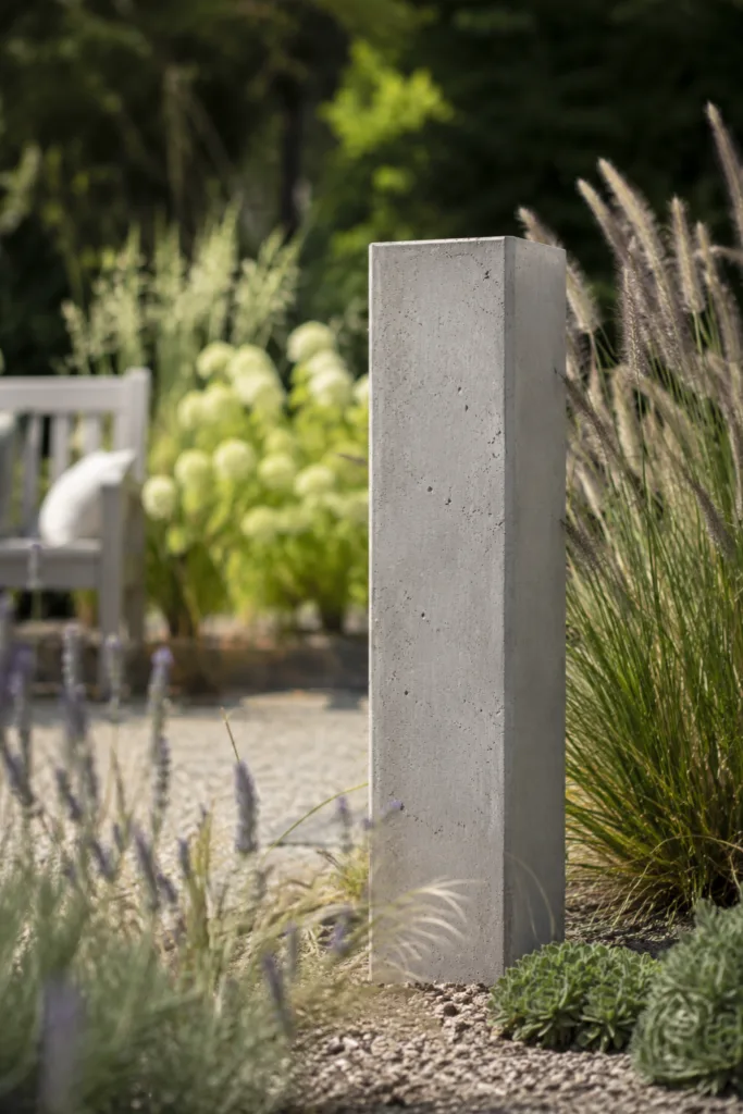 Gartendeko aus Beton mit moderner Betonstele zwischen Gräsern und Kiesfläche im Garten