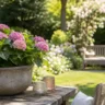 Deko für einen großen Garten im Juni mit Hortensien, Gartenbank und dekorativen Pflanzgefäßen.