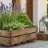 Gartendeko mit Holzkisten als bepflanzter Blickfang auf einer sonnigen Terrasse im naturnahen Garten.