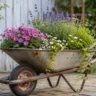 Gartendeko mit alter Schubkarre voller Blumen als dekorativer Blickfang im naturnahen Garten.