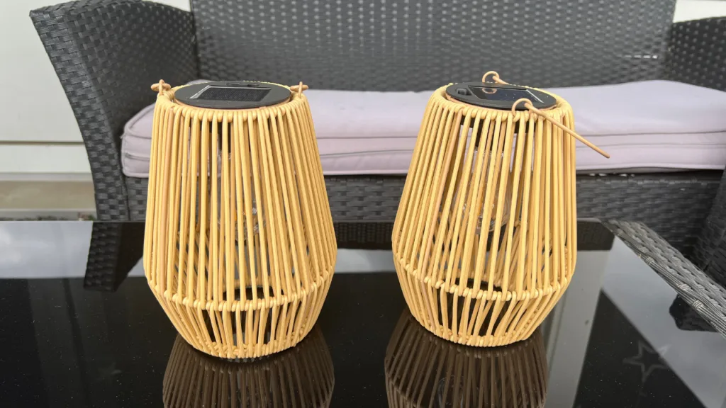 Warum diese Solar-Laternen aktuell zu meinen Gartenfavoriten gehören Zwei Solar-Laternen aus Rattan auf einem Gartentisch vor einer Lounge im Außenbereich.