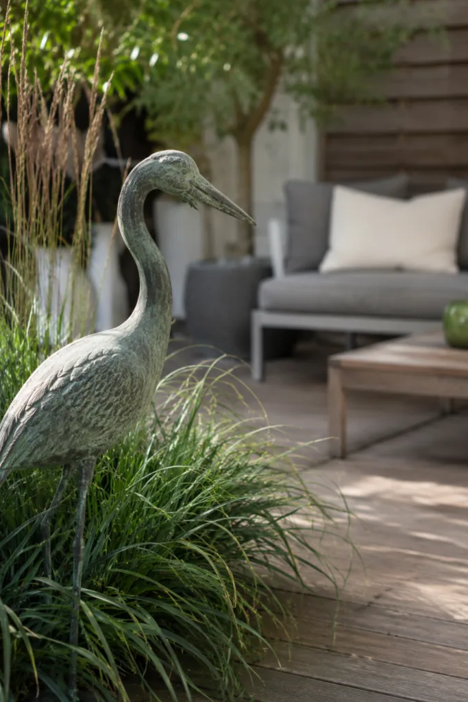 Terrassendeko mit Figuren: Reiherfigur zwischen Ziergräsern auf moderner Terrasse mit natürlicher Gartenatmosphäre.