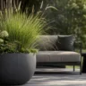 Moderne Sommerdeko für den Garten mit großem Pflanzgefäß, Gräsern und stilvoller Sitzecke.