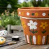 Gartendeko mit Kindern basteln: Bemalter Blumentopf und bunte Steine auf einem Holztisch im Garten.