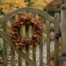 Herbstdeko fürs Gartentor mit Kranz, Laterne und Kürbis an einem rustikalen Holztor im Garten.