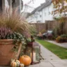 Herbstdeko für einen Reihenhausgarten mit Terrakottatopf, Heide, Ziergras, Laterne und Kürbissen auf der Terrasse.