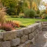 Herbstdeko für einen Terrassengarten mit Natursteinmauer, Kürbissen, Gräsern und herbstlicher Bepflanzung.