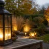 Herbstbeleuchtung im Garten mit leuchtender Laterne, warmen Lichtakzenten und herbstlichen Pflanzen am Abend.