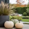 Moderne Herbstdeko für den Garten mit Gräsern, Kürbissen und Pflanzkübel auf einer stilvollen Terrasse.