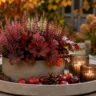 Moderne Herbstdeko für den Gartentisch mit Heide, Windlichtern, Zapfen und herbstlichem Garten im Hintergrund.