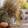 Pflegeleichte Herbstdeko für die Terrasse mit Kübel, Ziergras, Laterne und Kürbis auf Holzdeck.