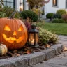 Halloweendeko im Vorgarten mit leuchtendem Kürbis, Laterne und herbstlicher Bepflanzung am Gartenweg.