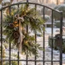 Winterdeko für Gartentor mit Tannengrün, Kranz, Schleife und warmen Lichtern an einem verschneiten Eingang.