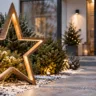 Moderne Weihnachtsdeko im Vorgarten mit beleuchtetem Stern, wintergrünen Pflanzen und elegantem Hauseingang.