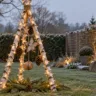 Drei Birkenstämme als Weihnachtsbaum auf dem Rasen mit Lichterkette, Holzsternen und Zapfen.