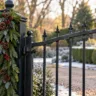 Schwarzes Metallgartentor mit grüner Weihnachtsgirlande, Tannenzapfen und roten Beeren am Torpfosten.