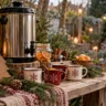 Rustikaler Holztisch mit Glühweintopf, Weihnachtstassen, Tannenzweigen und Laterne im winterlichen Garten.