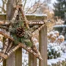 Großer Weihnachtsstern aus Birkenzweigen mit Tannengrün und Kiefernzapfen an einem verschneiten Holzzaun.