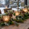 Langer Terrassentisch mit weihnachtlichem Gesteck aus Tannenzweigen, Zapfen, Holzsternen und leuchtenden Kerzen.