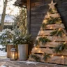 Weihnachtsbaum aus alten Palettenbrettern mit Lichterkette und Tannenzweigen vor einem Gartenhaus im Schnee.