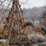 Große Pyramide aus Ästen mit warmweißen Lichtern und Naturanhängern in einem frostigen Gartenbeet.