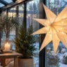 Weihnachtsdeko für den Wintergarten mit großem leuchtendem Papierstern am Fenster und winterlichem Gartenblick.