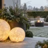 Moderne Weihnachtsdeko für den Garten mit Holzstern, Laterne und beleuchtetem Tannenbaum im Winter.